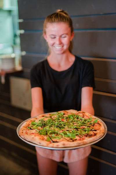 Smiling woman holding fresh baked pizza